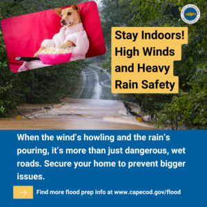 A graphic featuring a small dog wrapped in a pink blanket, holding a bowl of popcorn, with a background image of a flooded road surrounded by trees. The title reads "Stay Indoors! High Winds and Heavy Rain Safety," and the body text emphasizes staying safe during storms by securing your home and avoiding dangerous conditions. A link is provided for more flood prep information: www.capecod.gov/flood.